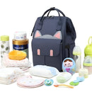 Bolsa Maternidade FlexiBag azul escuro com detalhes em rosa e itens de bebê ao redor